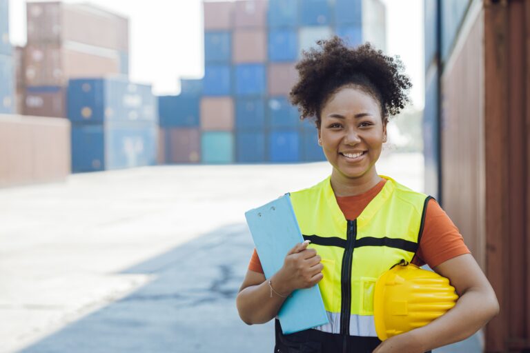 Employée femme portant son casque sous le bras dos à des conteneurs