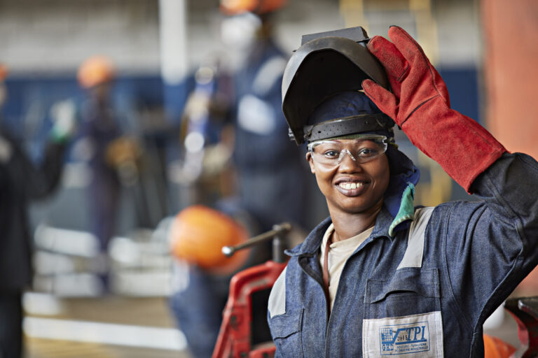 Une employée soudeuse qui dévoile son sourire en soulevant son casque de protection